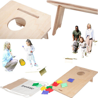 Plateau de jeu de cornhole pour enfants, en bois clair, avec un trou central et des pieds pliables. Des sacs de couleurs jaune, rouge, vert et bleu sont dispersés autour du plateau et un sac de rangement est visible. En arrière-plan, des enfants jouent so