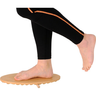 Un pied posé sur un plateau en bois de forme circulaire qui permet de travailler l'équilibre, avec une jambe levée et un pantalon noir avec des détails orange.