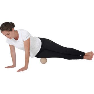 Femme effectuant un exercice de renforcement musculaire en position latérale, appuyée sur un ballon en bois, portant un t-shirt blanc et un pantalon noir, avec les mains posées au sol et les pieds nus.