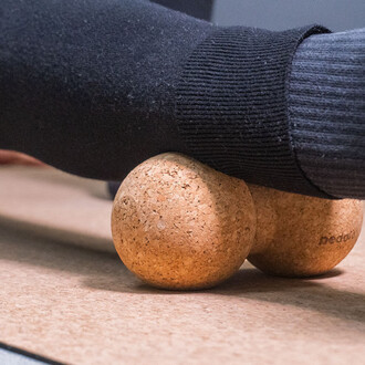 Un pied en chaussette noire reposant sur deux balles en liège sur un support en bois.