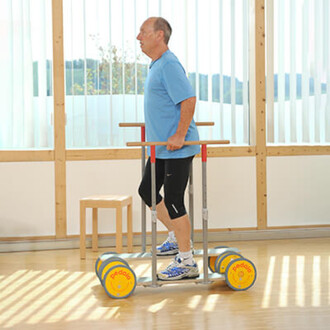 Un homme est en train d'utiliser les barres de rééducation Pedalo® dans une salle lumineuse. Il tient les barres avec ses mains, se tenant en équilibre, tandis qu'il marche sur un support avec des roues. Il porte un t-shirt bleu, un short noir, et des cha