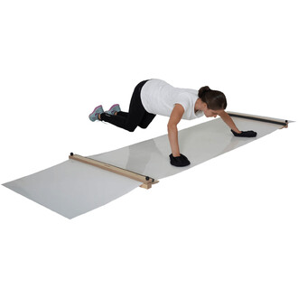 Femme en pleine exercice de jonglerie sur un tapis de jonglage. Elle est à genoux, les mains posées sur la surface glissante du tapis, portant des gants noirs. Elle porte un t-shirt blanc et des leggings noirs, avec des chaussures de sport. Le tapis est m