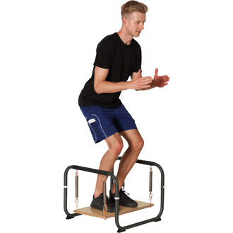 Homme en tenue de sport effectuant un exercice sur un appareil de fitness, debout sur une plateforme en bois entourée de ressorts, les bras en avant pour l'équilibre.