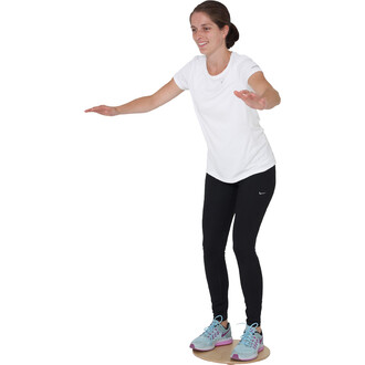 Femme en t-shirt blanc et leggings noirs, tenant les bras tendus pour l'équilibre, debout sur une planche de jonglerie. Elle a l'air concentrée et souriante, avec des chaussures de sport bleu clair et rose.