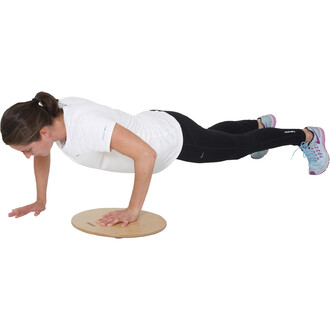 Femme en position de pompes sur un plateau en bois, portant un t-shirt blanc et un legging noir. Elle est concentrée, avec un regard vers le sol, et porte des chaussures de sport multicolores. Ses bras sont fléchis, et son corps est aligné horizontalement