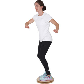 Femme en équilibre sur un pédalo Twister 380, portant un t-shirt blanc et un legging noir, avec des chaussures de sport colorées, effectuant une posture de stabilité.