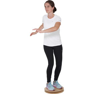 Femme debout sur un plateau de jonglerie Pedalo® Twister 380, les bras écartés pour maintenir l'équilibre, vêtue d'un t-shirt blanc et de leggings noirs, avec des chaussures de sport bleu clair et violette. Fond blanc.