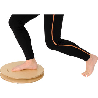 Un pied nu se tient sur un appareil d'équilibre en bois appelé Pedalo® Twister 380, tandis qu'une jambe est fléchie. La personne porte un pantalon noir avec une bande orange sur le côté. L'image met en avant l'utilisation de l'appareil pour des exercices 