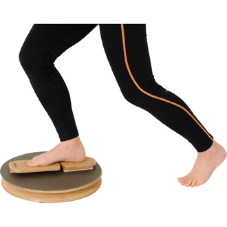 Personne en train d'utiliser le Pedalo® Twister 380, se tenant sur une plateforme circulaire. Un pied est posé sur la partie en bois de la planche, tandis que l'autre pied est à l'extérieur de la planche. La personne porte des leggings noirs avec une band