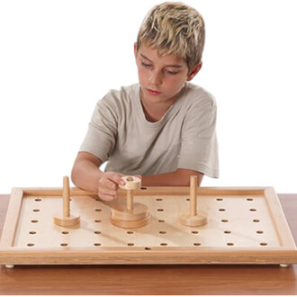 Un enfant concentré, portant un t-shirt gris, manipule un disque en bois sur un plateau en bois avec des trous. Le plateau comporte trois poteaux en bois de différentes hauteurs.