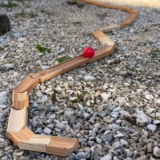 Balancier en bois sinueux avec une balle rouge placée sur une surface en gravier.