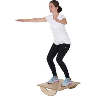 Femme en t-shirt blanc et legging noir, en équilibre sur une planche de balance, les bras tendus devant elle. Elle porte des chaussures de sport bleu et rose. Fond blanc.