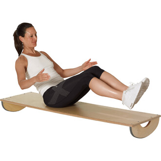 Femme en tenue de sport, assise sur une planche de jonglerie, effectuant un exercice de renforcement abdominal. Elle porte un haut sans manches blanc et un legging noir, et ses jambes sont fléchies, pieds levés. Le fond est blanc, mettant en avant l'activ