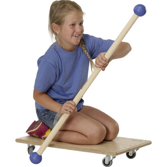 Une jeune fille souriante assise sur une planche à roulettes, tenant un bâton en bois avec une extrémité bleue. Elle porte un t-shirt bleu et un short en jean. La planche est munie de roulettes et la fille semble s'amuser avec le matériel de jonglerie.