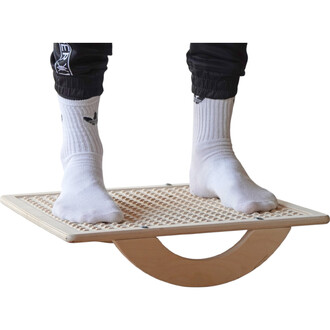 Plateforme de jonglerie en bois avec deux pieds nus se tenant dessus, sur un support en forme de demi-cercle. Le sol est recouvert d'un matériau en relief, tandis que la personne porte des chaussettes blanches.