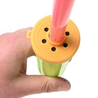 Vue rapprochée de la pompe à ballons Pocket Balloon Double Action: embout jaune circulaire à trous avec tube rose inséré, tenu par une main.