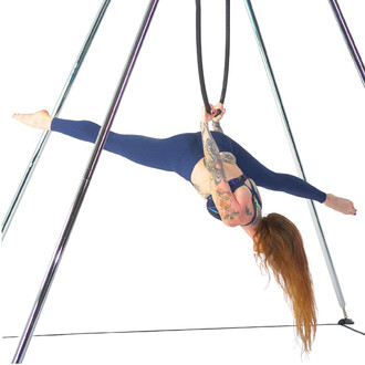 Une personne effectue une pose de yoga sur un portique, suspendue par un cerceau. Elle est vêtue d'un legging bleu et se penche en avant, un bras tenant le cerceau tandis que l'autre est tendu. Ses longs cheveux roux tombent vers le bas et elle a des tato