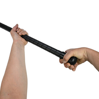 Main tenant un quillon pour Acro Staff Gora, montrant une prise ferme sur le bâton noir texturé, avec une autre main en soutien. Le fond est blanc.