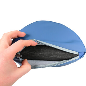 Repose Tête Sarneige vu de près, avec une main tenant le dessus d'une housse bleue zippée. L'intérieur est rembourré de mousse noire, offrant un confort optimal.