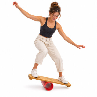 Una donna sorridente si mantiene in equilibrio su una tavola di legno per Rola Bola con un rullo rosso, con le braccia tese per maggiore stabilità.