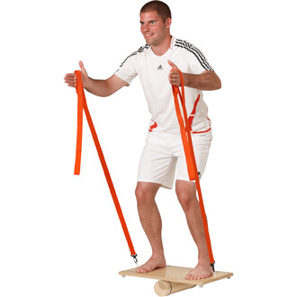 Homme pratiquant l'équilibre sur une planche avec des sangles orange, pieds nus, portant un t-shirt blanc et un short blanc. Il tient les sangles avec les deux mains, affichant un sourire, et se trouve sur un support en bois.