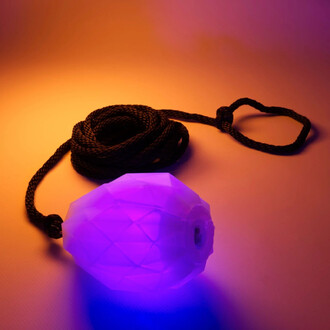 Rope Dart LED Prism de Threeworlds : une corde noire enroulée avec un dart lumineux en forme de diamant qui émet une douce lumière violette sur un fond dégradé allant du violet à l'orange.