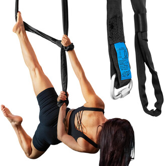 Image d'une personne en position aérienne sur des sangles noires, tenant les sangles avec les mains tout en étant suspendue. Les sangles sont équipées d'un mousqueton et présentent une étiquette bleue avec des spécifications de sécurité. La personne porte