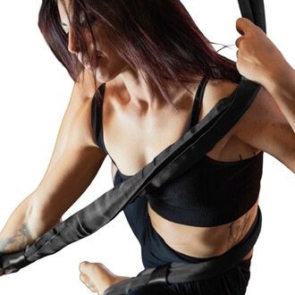 Femme en action utilisant des sangles aériennes, vêtue d'un débardeur noir, montrant une technique de jonglage aérien. Les sangles sont maintenues dans ses mains tandis qu'elle s'accroche avec une position élégante, mettant en avant sa concentration et sa