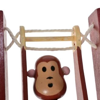Singe en bois acrobate suspendu à un fil, avec un visage souriant et des oreilles arrondies, sur un cadre en couleur rouge.