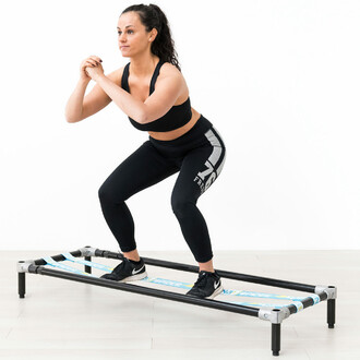 Femme effectuant un exercice de squat sur la structure autoportante SlackGYM avec deux slacklines élastiques, démontrant l'entraînement à l'équilibre et à la stabilité du tronc.
