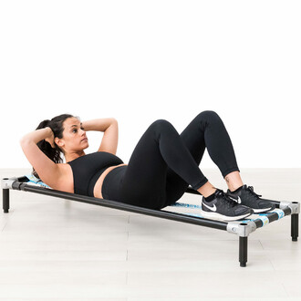 Femme effectuant un exercice de crunch sur la structure autoportante SlackGYM avec slacklines élastiques, illustrant l'entraînement des abdominaux et le renforcement de la stabilité du tronc.