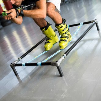 Homme en chaussures de ski effectuant un exercice de flexion sur la slackline élastique de la structure autoportante SlackGYM, illustrant l'utilisation de l'équipement pour l'entraînement à l'équilibre et la préparation physique spécifique au ski.