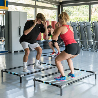 Groupe de personnes effectuant des exercices de squat sur des structures autoportantes SlackGYM dans une salle de sport, montrant l'entraînement à l'équilibre et au renforcement musculaire en groupe.
