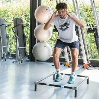 Homme effectuant un exercice de squat sur une structure autoportante SlackGYM dans une salle de sport, démontrant l'entraînement à l'équilibre et au renforcement musculaire.