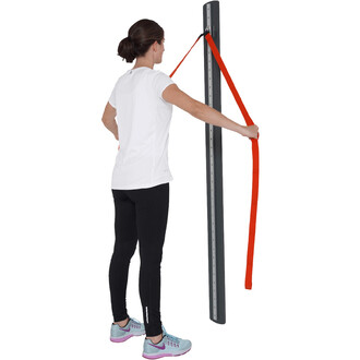 Femme debout en t-shirt blanc et leggings noirs, utilisant un équipement de jonglerie, tenant une sangle orange attachée à un poteau vertical. Elle effectue un exercice de traction ou de renforcement. Des chaussures de sport bleu clair avec des détails ro