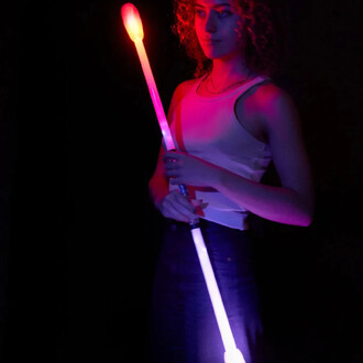 Femme tenant un staff lumineux rechargeable, émettant des lumières rouge et violet, sur fond noir. Elle porte un débardeur blanc et a les cheveux bouclés.