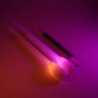 Trois staffs lumineux rechargeables au design élégant, disposés sur un fond violet. Les deux bâtons en silicone émettent une lueur multicolore, tandis qu'un tube transparent avec une décoration sombre est visible en arrière-plan. L'ambiance générale est d