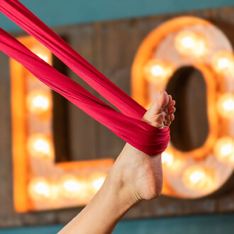 Tissu aérien rouge enroulé autour d'un pied, avec un fond décoré de lettres lumineuses.