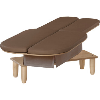 Table de massage en bois avec un revêtement en simili cuir brun, dotée de deux parties pliables pour un confort optimal. Légèrement surélevée sur des pieds en bois clair, elle présente un espace de rangement en dessous avec un tissu gris.