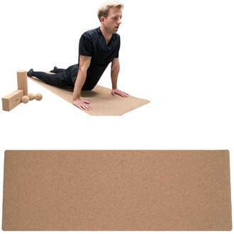 Un homme en position de yoga sur un tapis en liège, entouré de divers accessoires de yoga (deux blocs et deux balles en liège). Le tapis est de couleur beige et le sol est clair. L'homme porte un vêtement noir et semble concentré sur sa pratique.