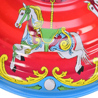 Illustration colorée d'une toupie en métal avec un motif de manège, représentant un cheval blanc avec une selle verte et des détails vifs, sur un fond rouge. Des ornements dorés et un motif de boule bleue complètent le design.