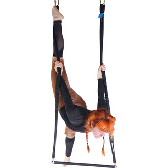 Acrobate suspendue sur un trapèze Prodigy Polysafe, tenant les sangles noires, barre du trapèze en dessous, cheveux roux flamboyants.