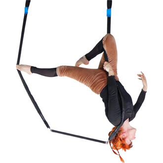 Trapèze aérien Prodigy Polysafe : artiste suspendue en position inversée sur une trapèze en tissu noir, sangles noires avec embouts bleus, vêtue d’un haut noir et d’un pantalon brun.