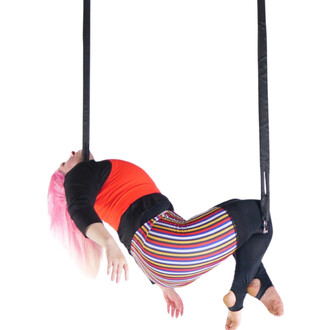 Artiste aérienne suspendue sur trapèze Prodigy Polysafe, accrochée par deux sangles noires, en position inversée, vêtue d’un haut rouge et d’un pantalon à rayures multicolores, cheveux roses.