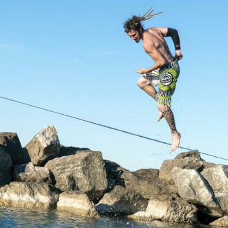 Spin jump on a slackline over the sea with rocks in the background.