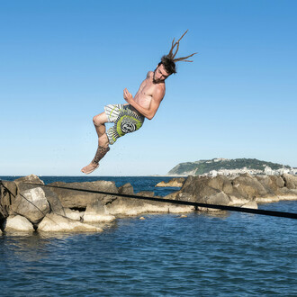 Crazy guy jumping and spinning in the air. Above a slackline over the ocean