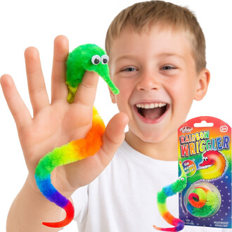 Un jeune garçon souriant tient une créature en peluche colorée, ressemblant à un ver, sur sa main. La créature est principalement verte avec des nuances de rouge, jaune, et bleu, représentant un arc-en-ciel. À côté de lui, on voit l'emballage du produit V