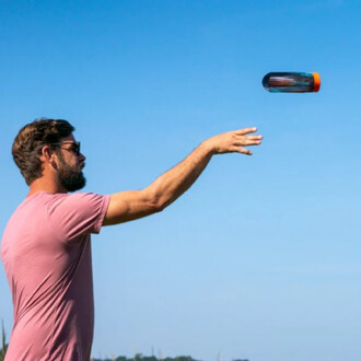 Homme en t-shirt rose lançant le Waboba Airlyft sous un ciel dégagé. Le jouet est en vol, avec un fond de paysage naturel.