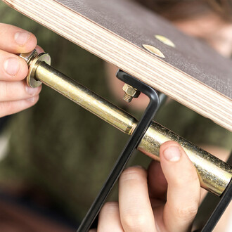 Image montrant une main en train de fixer une planche en bois sur la structure de slackline avec des vis dorées. L'image met en évidence la solidité et la qualité du montage de la structure de slackline.