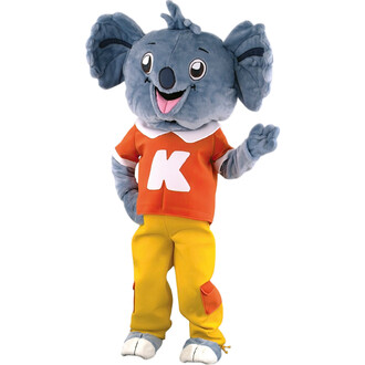 Mascotte représentant un koala avec une grande tête, un sourire joyeux, des yeux brillants et des oreilles caractéristiques. Elle porte un t-shirt orange avec un K blanc et des pantalons jaunes. La mascotte fait un geste de la main, évoquant l'amitié et l